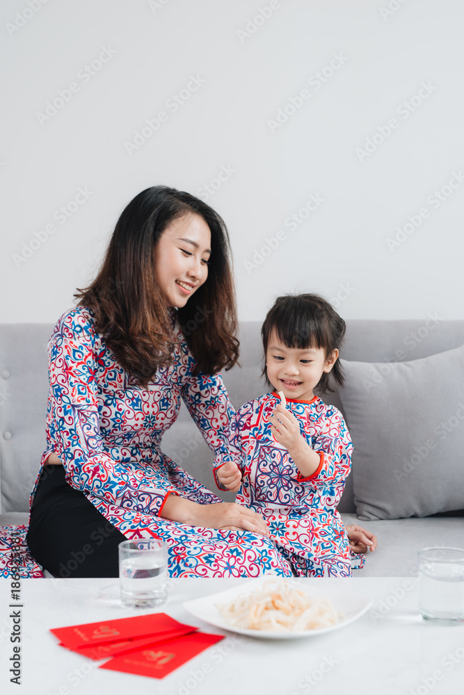 Vietnamese mother and daughter in Ao Dai Traditional dress, celebrate new year at home. Tet Holiday.