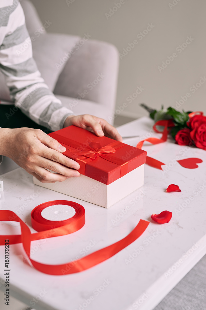 Male hands wrapping Valentine handmade present in paper with red ribbon