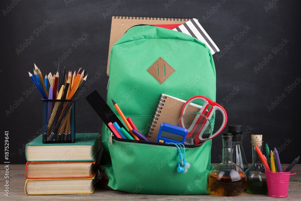 Education concept - school backpack with books and other supplies, blackboard background