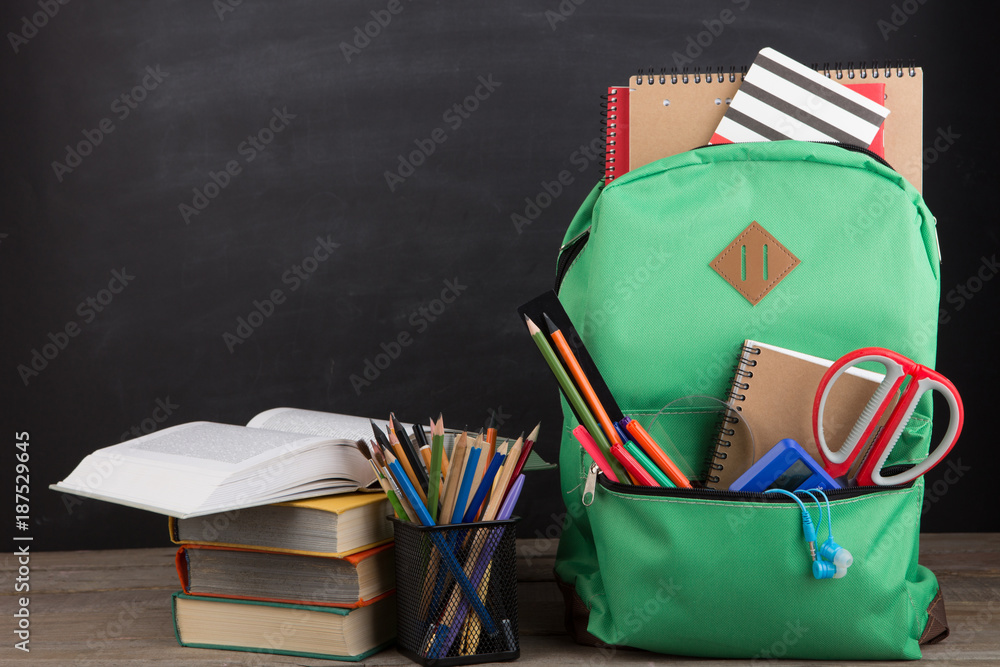 Education concept - school backpack with books and other supplies, blackboard background