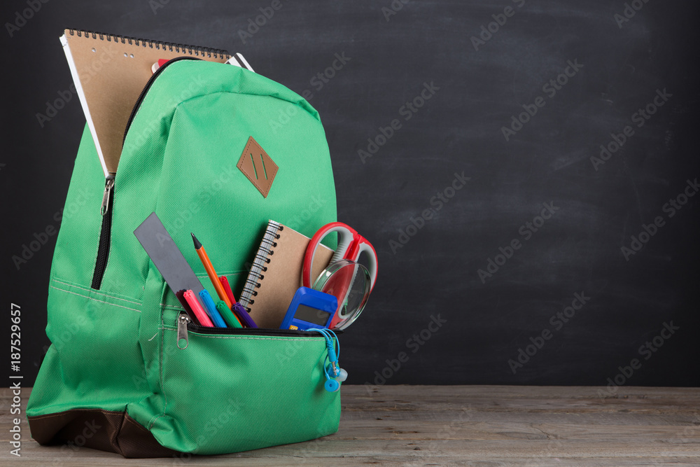 Education concept - school backpack with books and other supplies, blackboard background