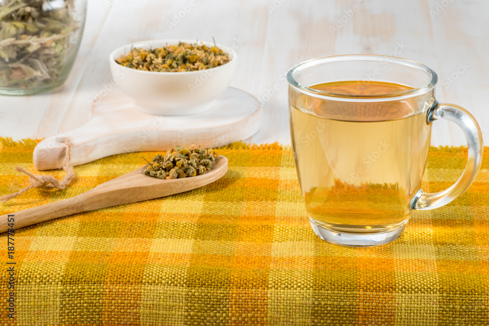 Cup of chamomile tea with dry chamomile flowers  on white wooden background.