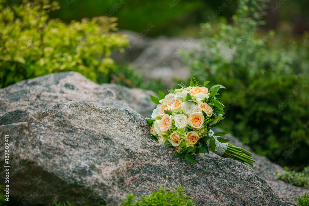 Wedding bouquet of flowers and greenery with ribbon lies on a rock on a background of greenery. Wedd