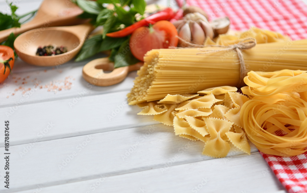 Pasta spaghetti, farfalle, linguine with vegetables and spices on white wooden table