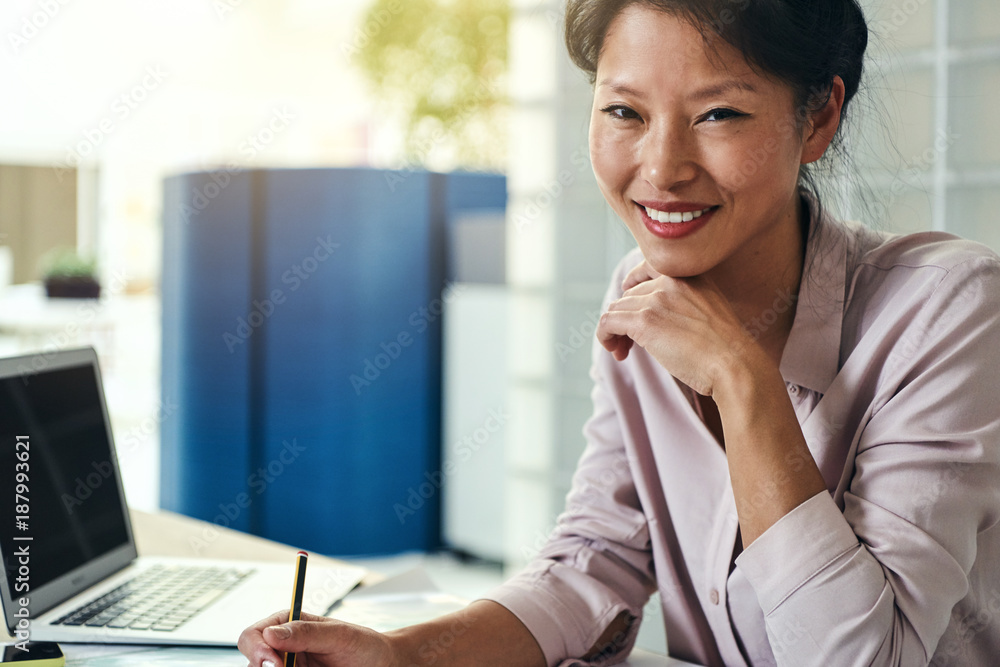 Smiling Asian designer working at her desk in an office