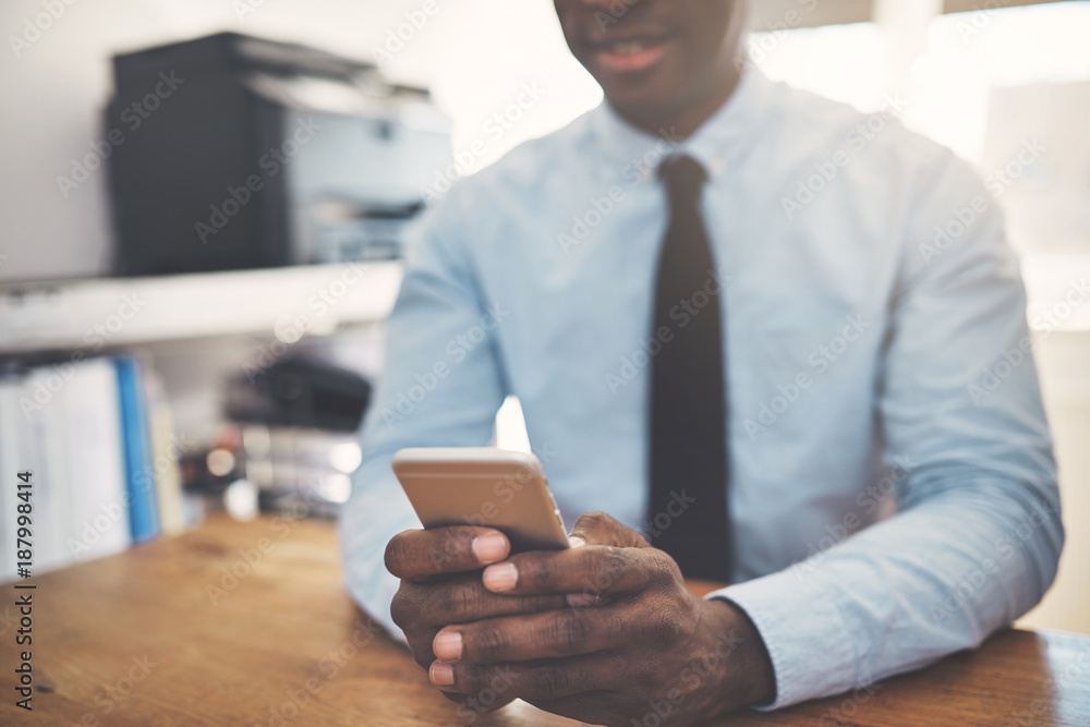 African businessman sending texts on a cellphone in an office