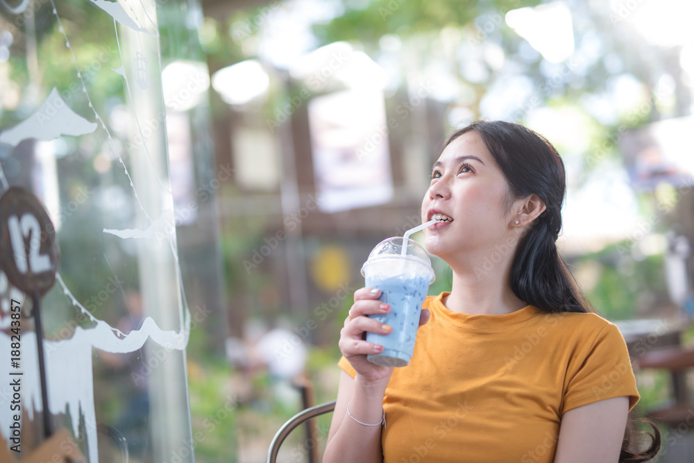 年轻的亚洲女人在咖啡店喝冰牛奶，抬头看