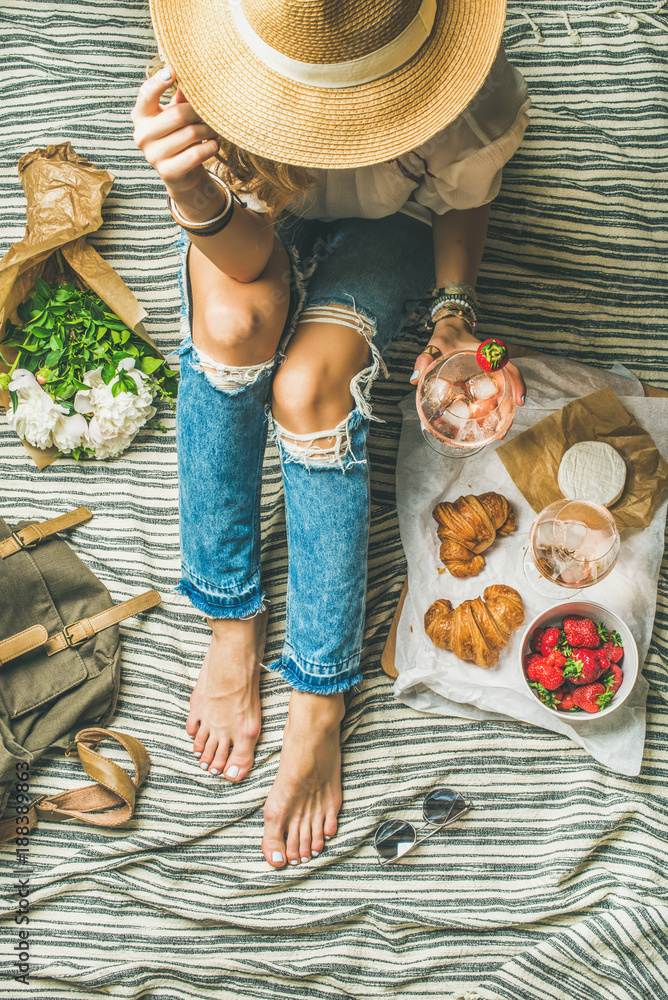 French style romantic picnic setting. Woman in shabby jeans with glass of ice rose wine, strawberrie