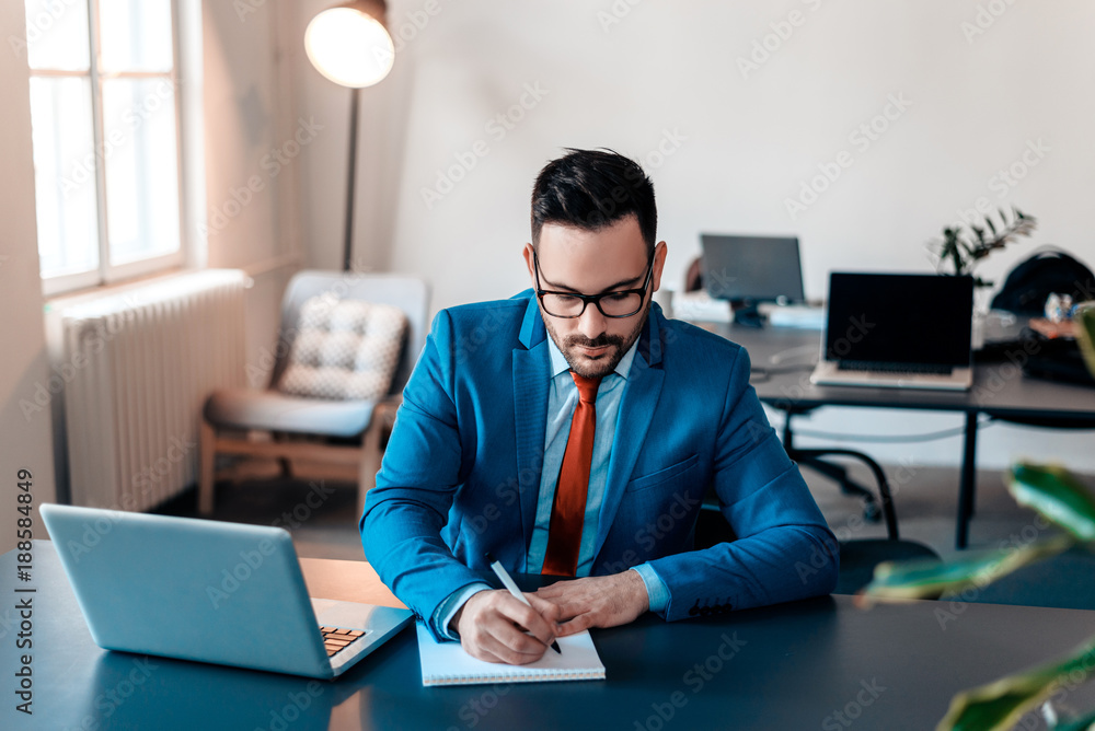 Young handsome businessman writing notes on paper in modern office.