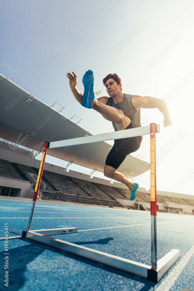 Athlete jumping over an hurdle on running track