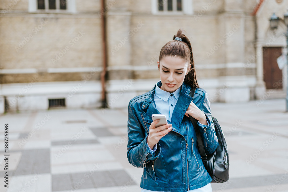 Beautiful young woman with backpack using phone at city street.