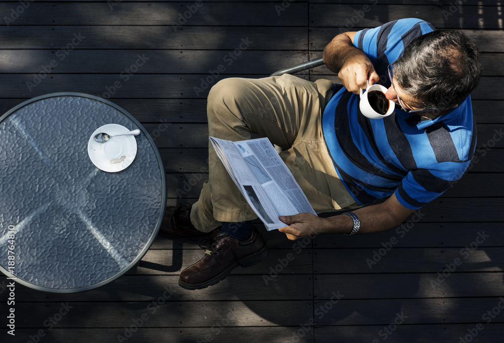 Man relaxing while reading a newspaper and drinking coffee