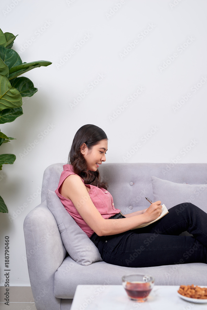 Pretty asian woman writing on couch at home in the living room