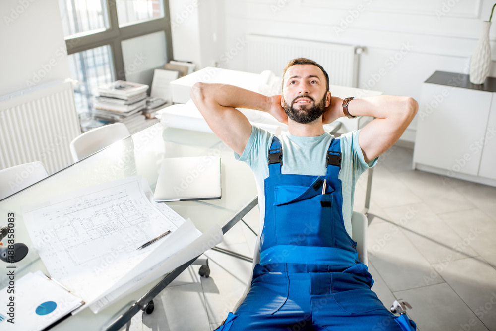 Portrait of a handsome repairman in workwear relaxing after the work in the office with laptop and p