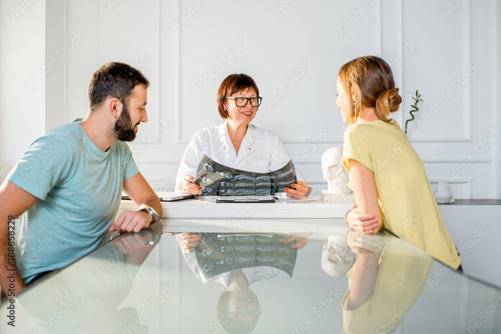 Young couple having a consultation with senior doctor discussing x-ray print sitting in the white of