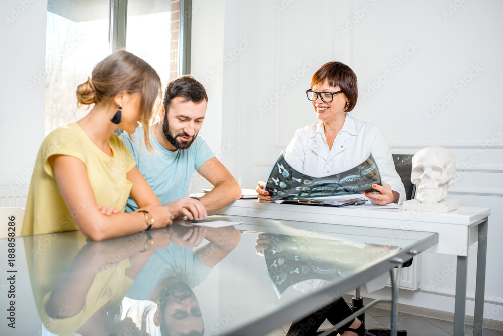 Young couple having a consultation with senior doctor discussing x-ray print sitting in the white of