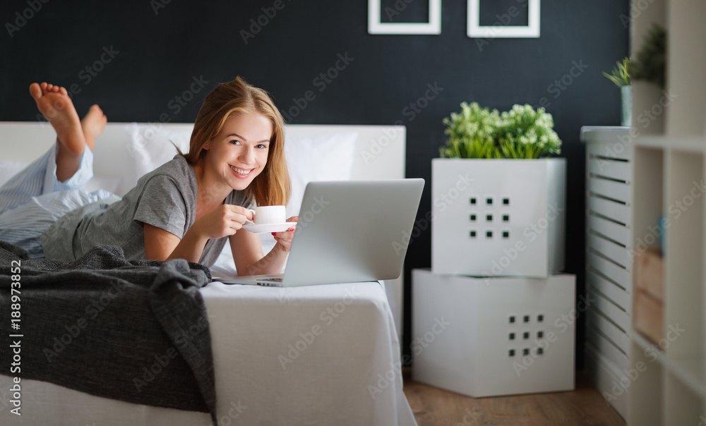 年轻漂亮的女人，早上在床上拿着笔记本电脑和一杯咖啡