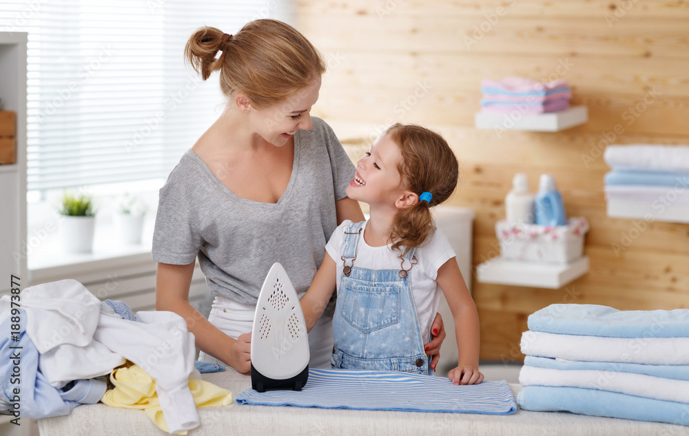 Happy family mother housewife and child daughter ironing clothes   in laundry