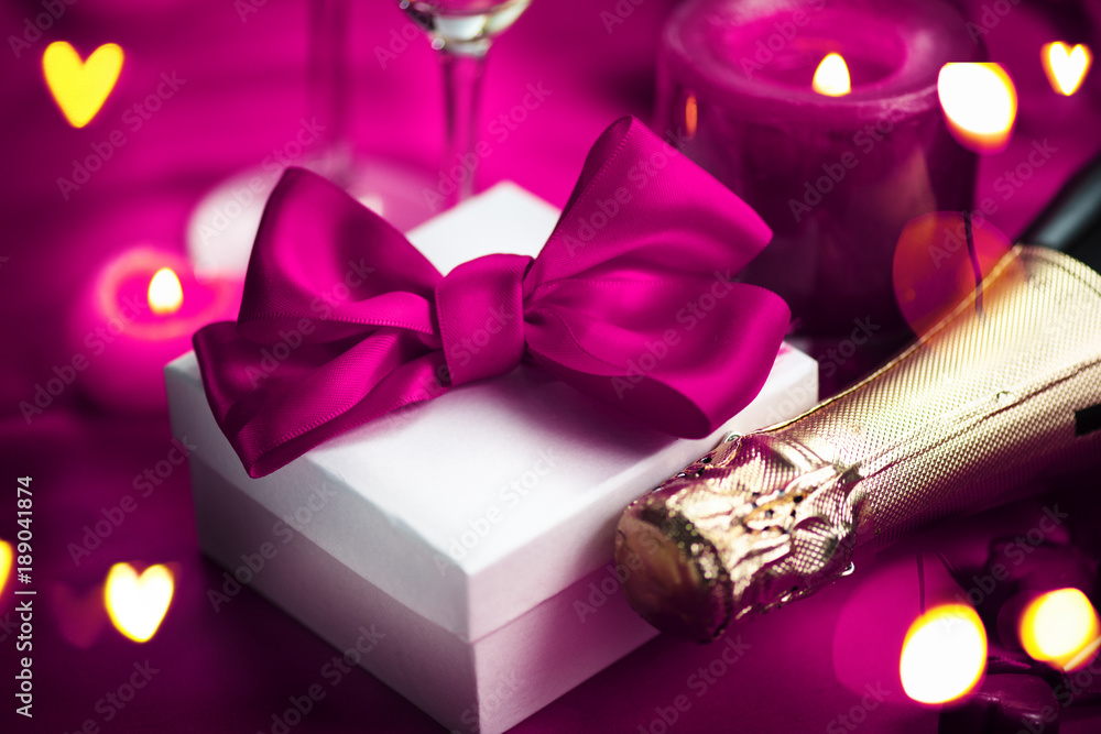 Valentines Day romantic dinner. Champagne, candles and gift box over holiday purple background