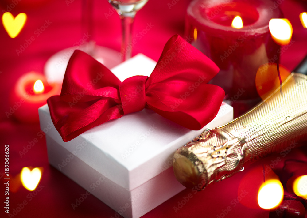 Valentines Day romantic dinner. Champagne, candles and gift box over holiday red background