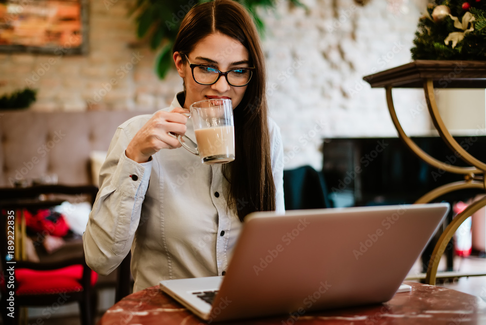 Beautiful long haired girl drinking coffee while looking at laptop.