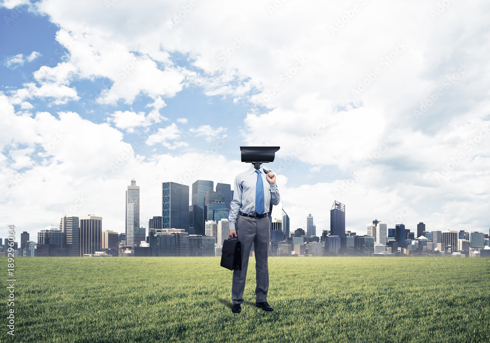 Camera headed man standing on green grass against modern citysca