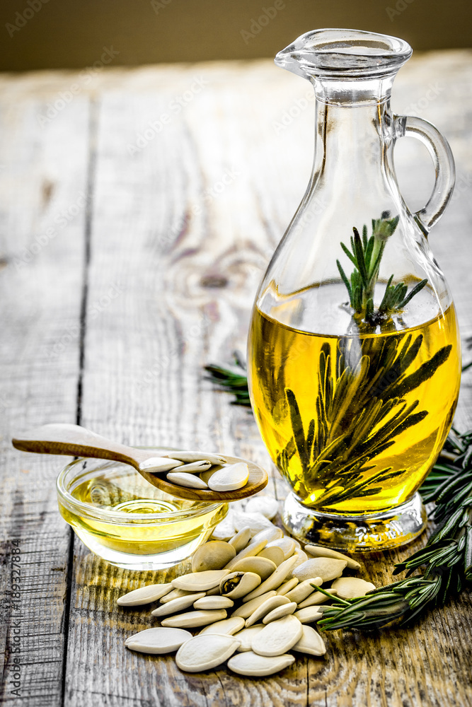 oil in carafe with pepitas and rosemary on wooden background