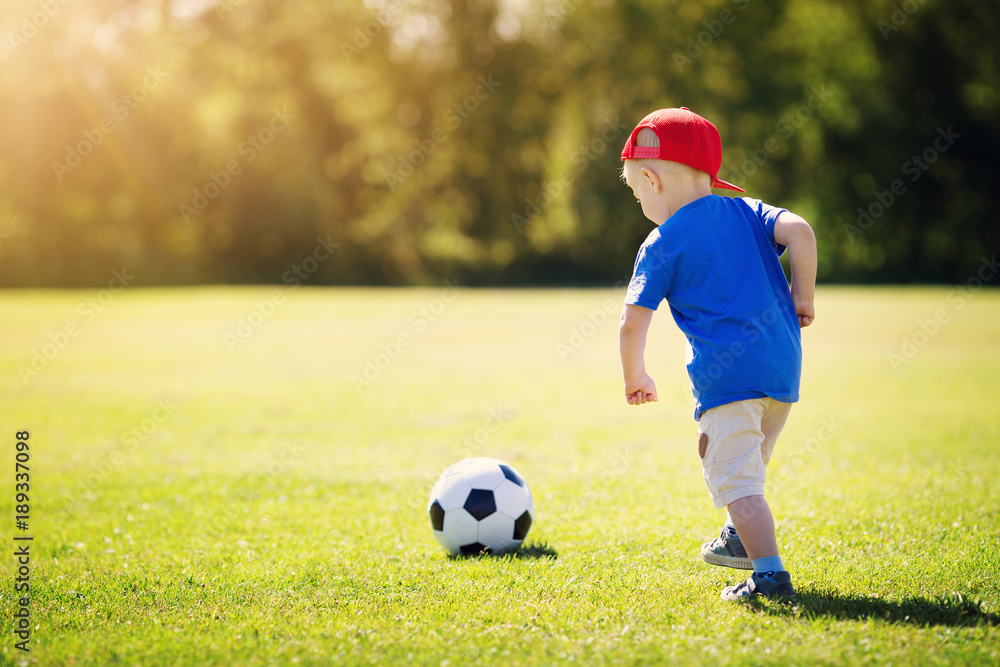 Little boy playing football on the field with gates