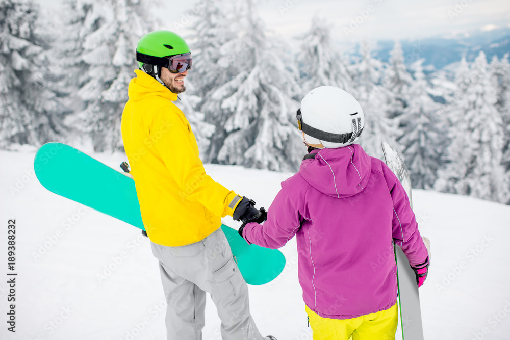 Young couple walking with snowboards during the winter vacation on the snowy mountains