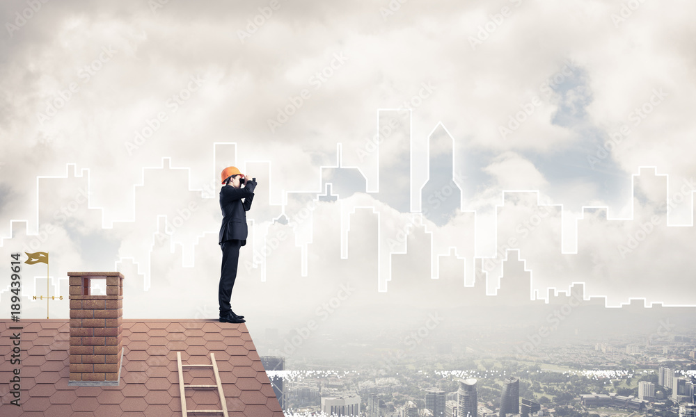 Engineer man standing on roof and looking in binoculars. Mixed m