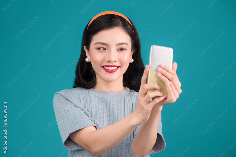 Close-up of smiling lovely pinup asian girl taking selfie photo over blue background.