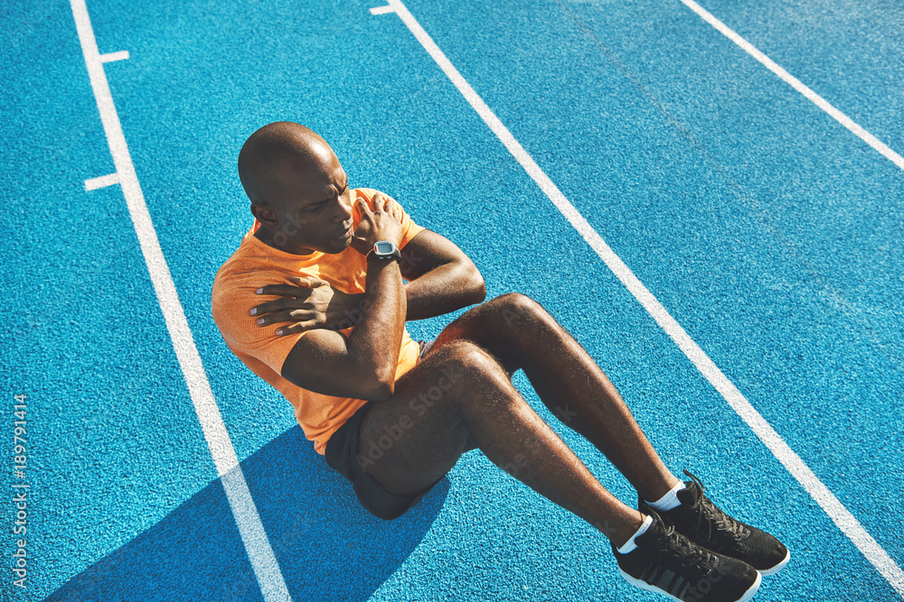 Fit young athlete doing crunches on a track outside