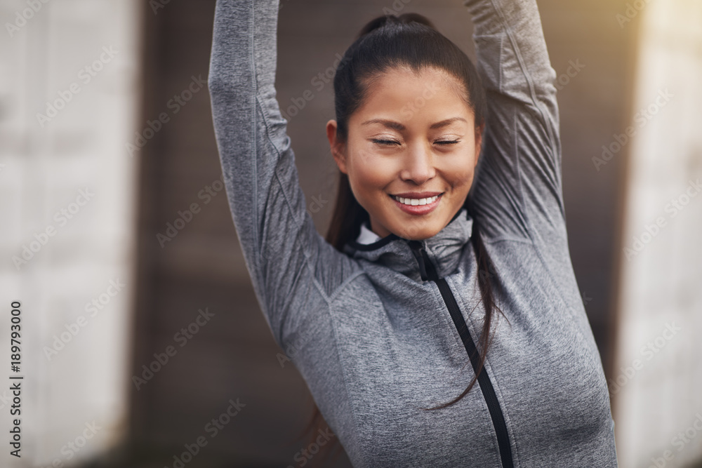 Fit young Asian woman smiling and stretching before a jog