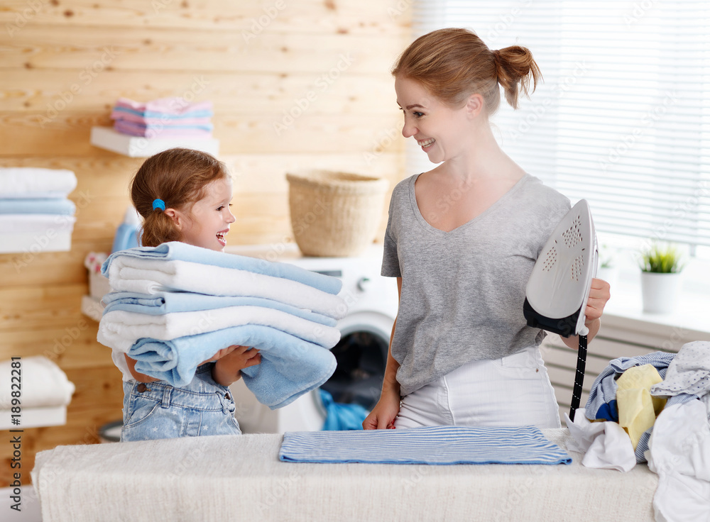 Happy family mother housewife and child daughter ironing clothes   in laundry