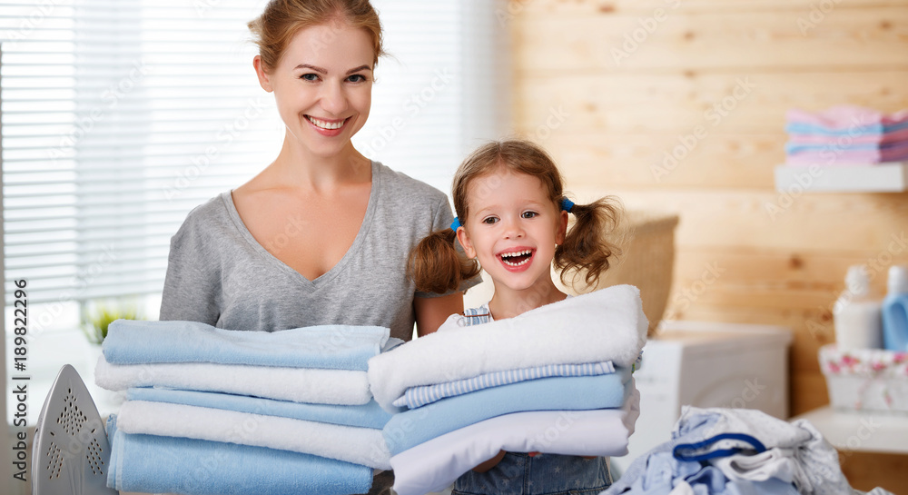 Happy family mother housewife and child daughter ironing clothes   in laundry