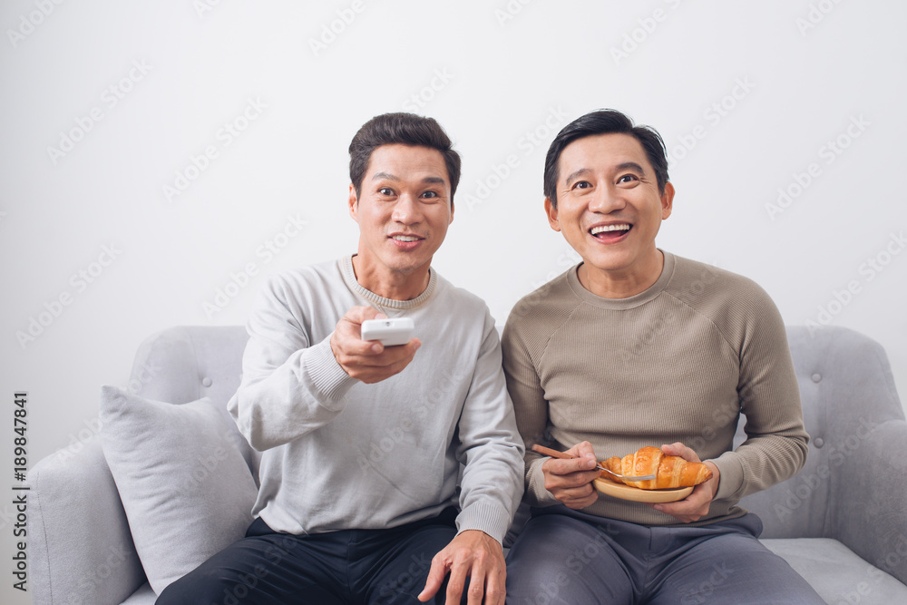 Two male friends watching football sitting on sofa at home