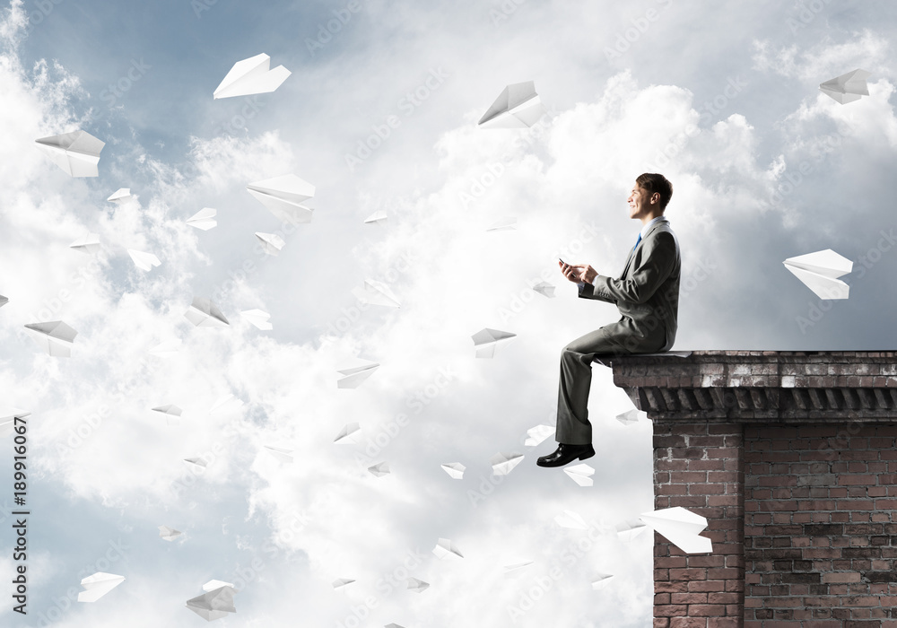 Man on roof edge send message with smartphone and cityscape at background