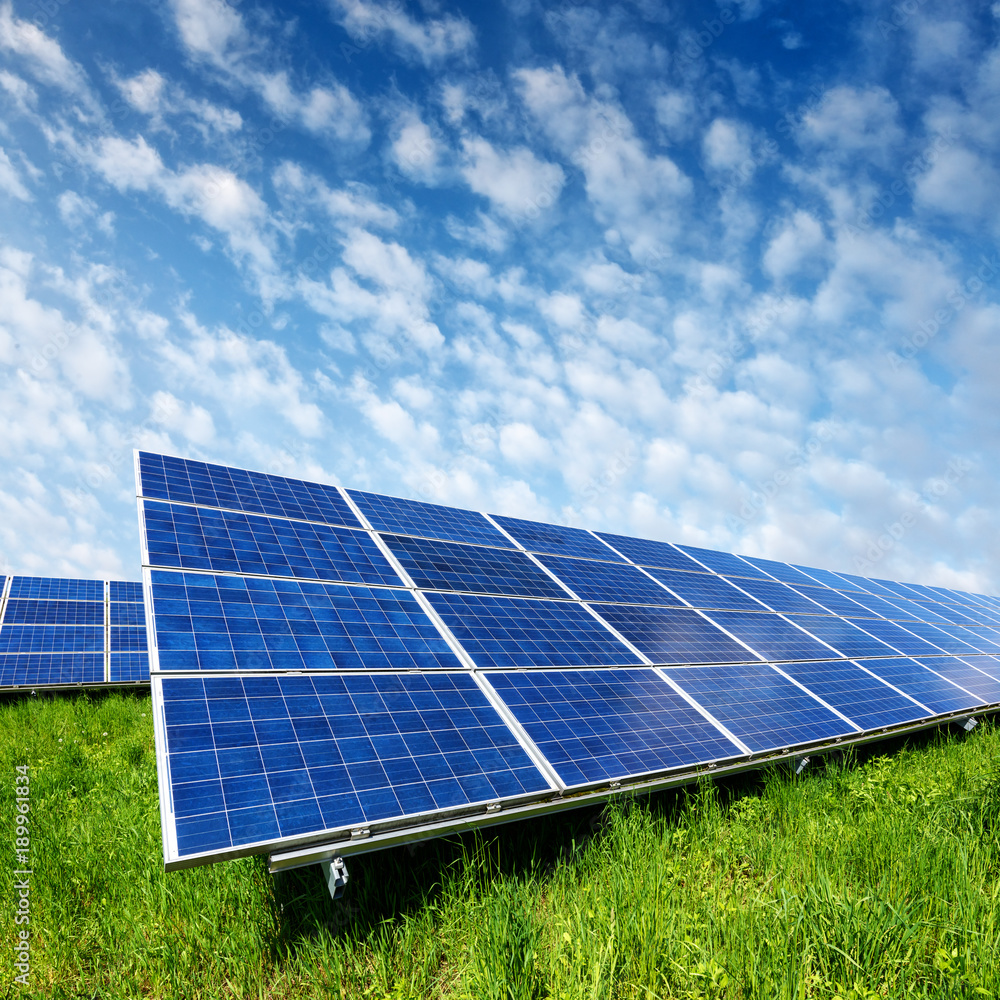 Solar panel on blue sky background. Green grass and cloudy sky. Alternative energy concept