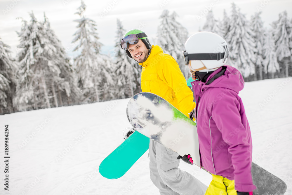 Young couple walking with snowboards during the winter vacation on the snowy mountains