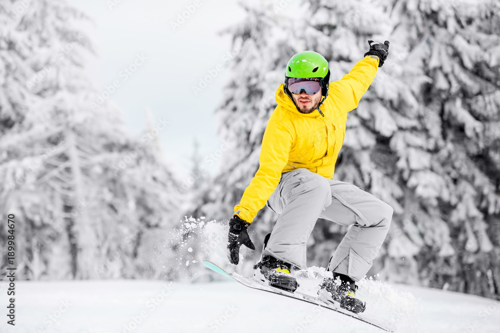 穿着五颜六色运动服的男子在有美丽树木的雪山上滑雪板跳跃