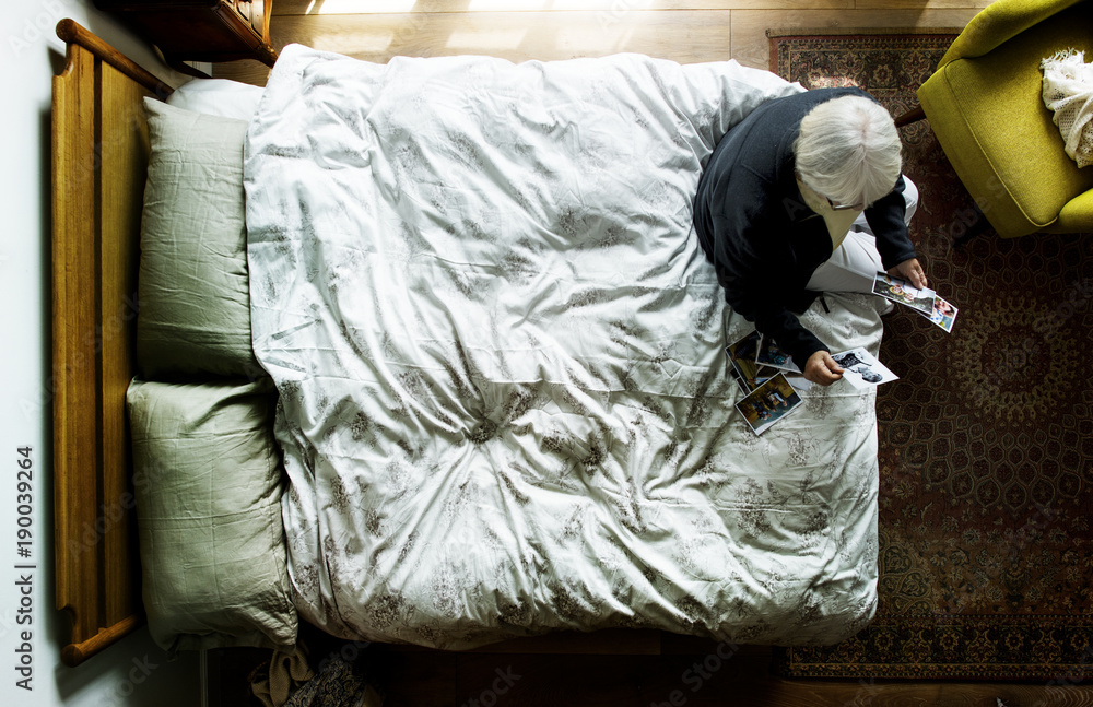 Elderly Caucasian sitting on the bed looking at photos