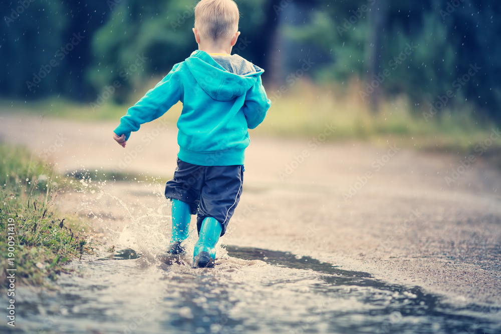 雨天孩子穿着雨鞋在水坑里行走