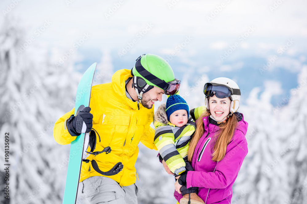 一个幸福的家庭的肖像，穿着冬季运动服的男婴站在滑雪板上