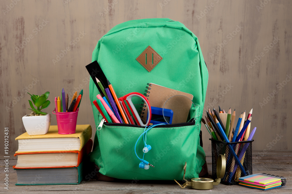 Education concept - school backpack with books and other supplies on the desk