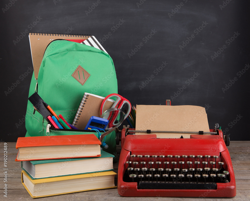 Education concept - school backpack with books and other supplies, blackboard background