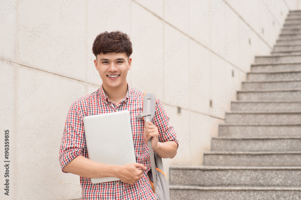 亚洲大学生在校园里拿着笔记本电脑