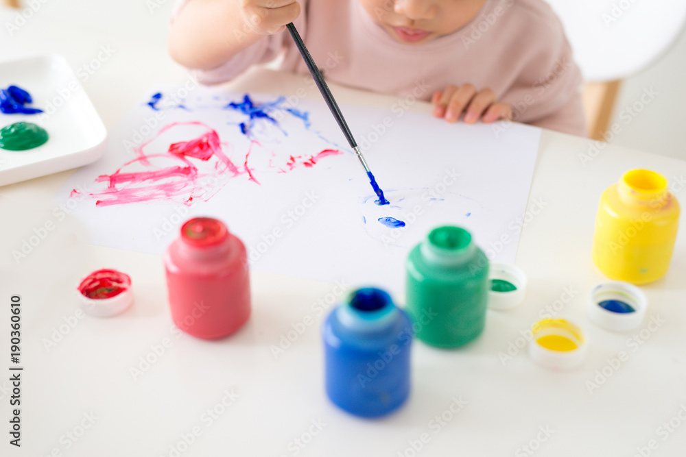 Little asian girl painting with paintbrush and colorful paints