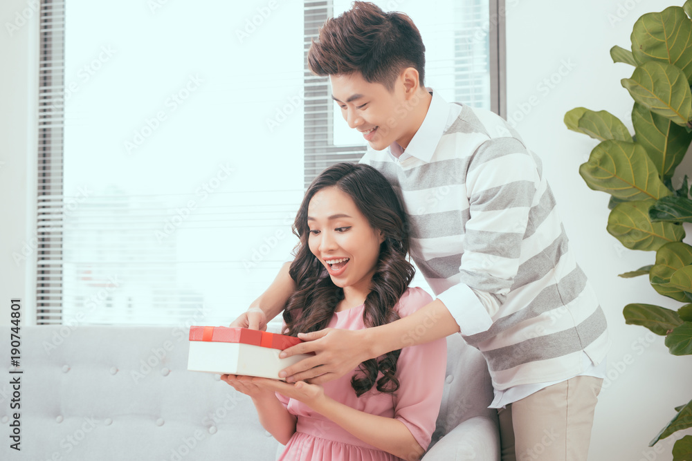 Young couple opening parcel gift box on the couch