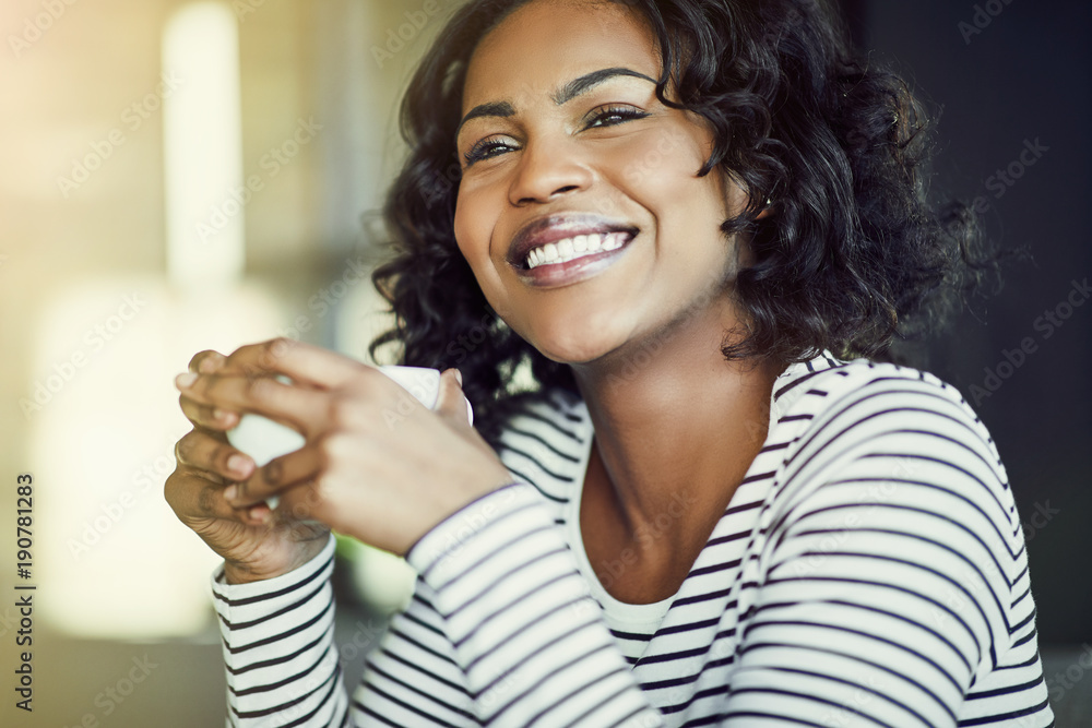 Young African woman laughing while enjoying coffee in a cafe