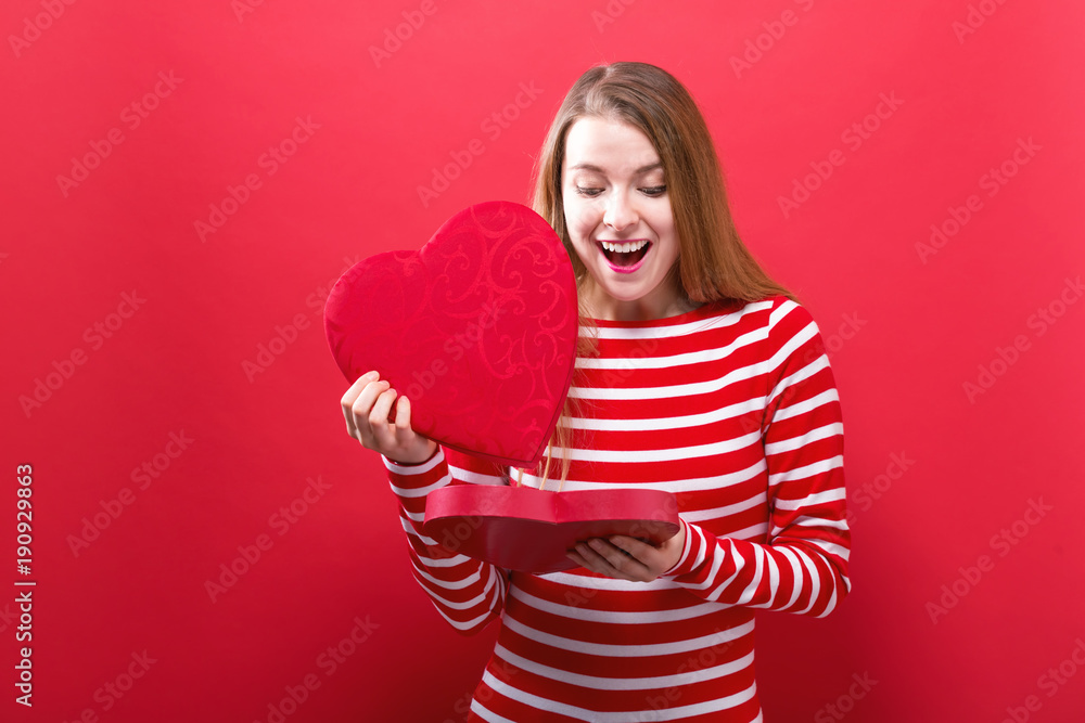 Happy young woman holding a big heart gift box on a red background